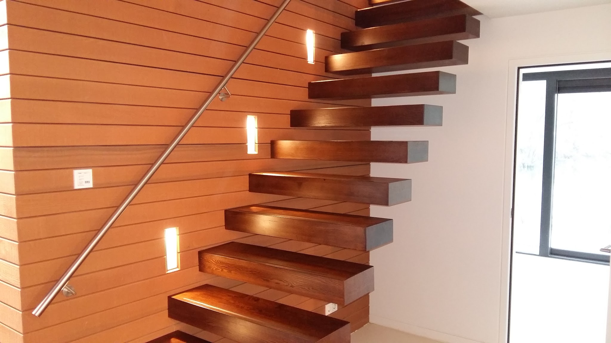 Zwevende trap met massieve houten treden langs een wand met houten delen